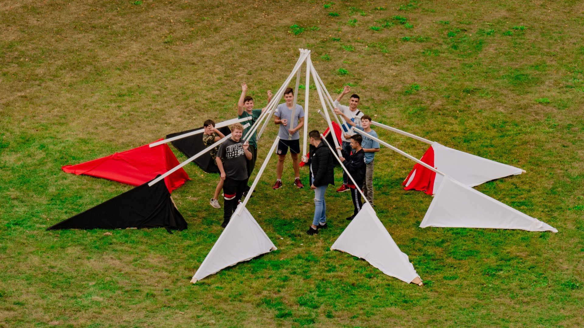 Eine Gruppe Schüler baut eine Holzkonstruktion auf einer Wiese.