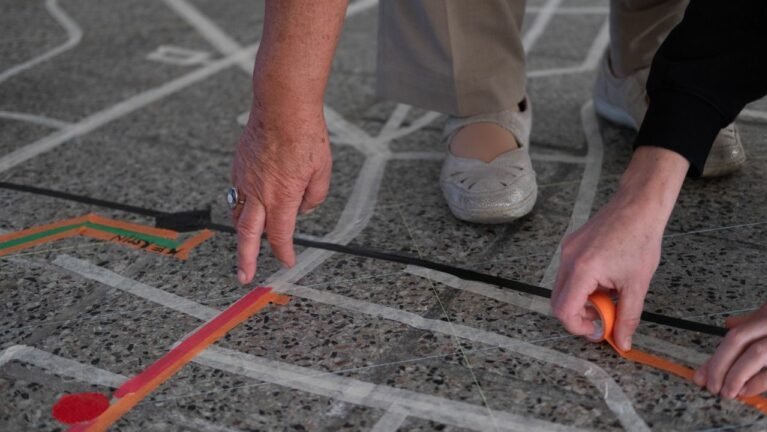 Zwei Personen formen mit Klebeband ein Muster auf dem Boden.