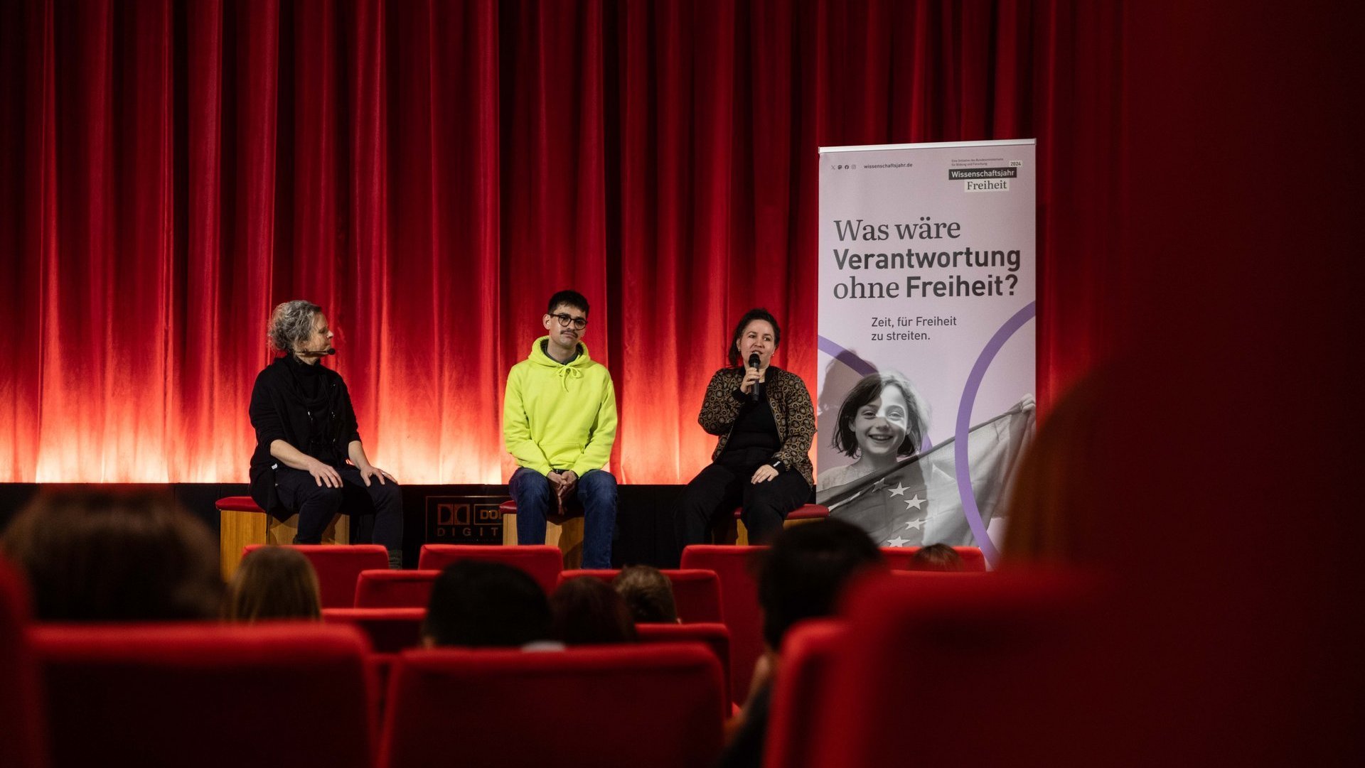 Eine Gesprächsrunde aus drei Menschen in einem Kinosaal.