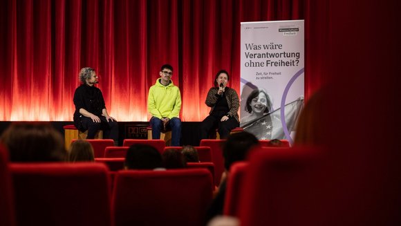 Eine Gesprächsrunde aus drei Menschen in einem Kinosaal.