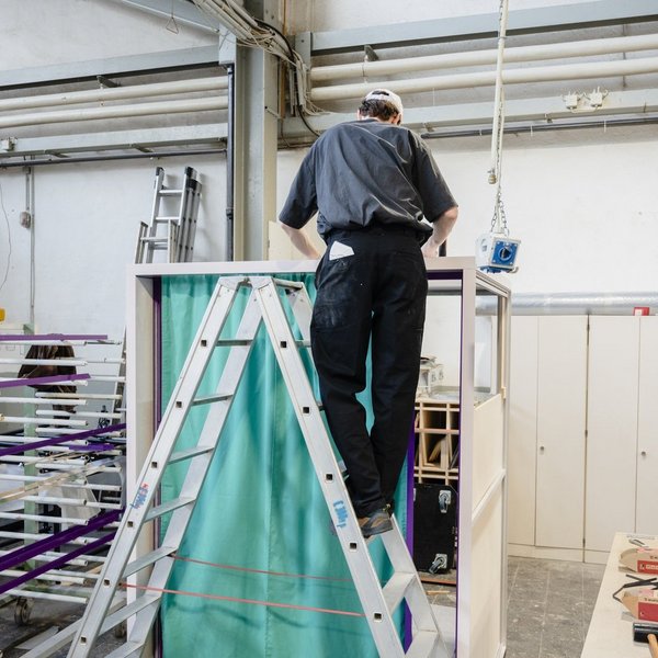Eine Person steht auf einer Leiter vor der Erzählbox und befestigt den Vorhang.