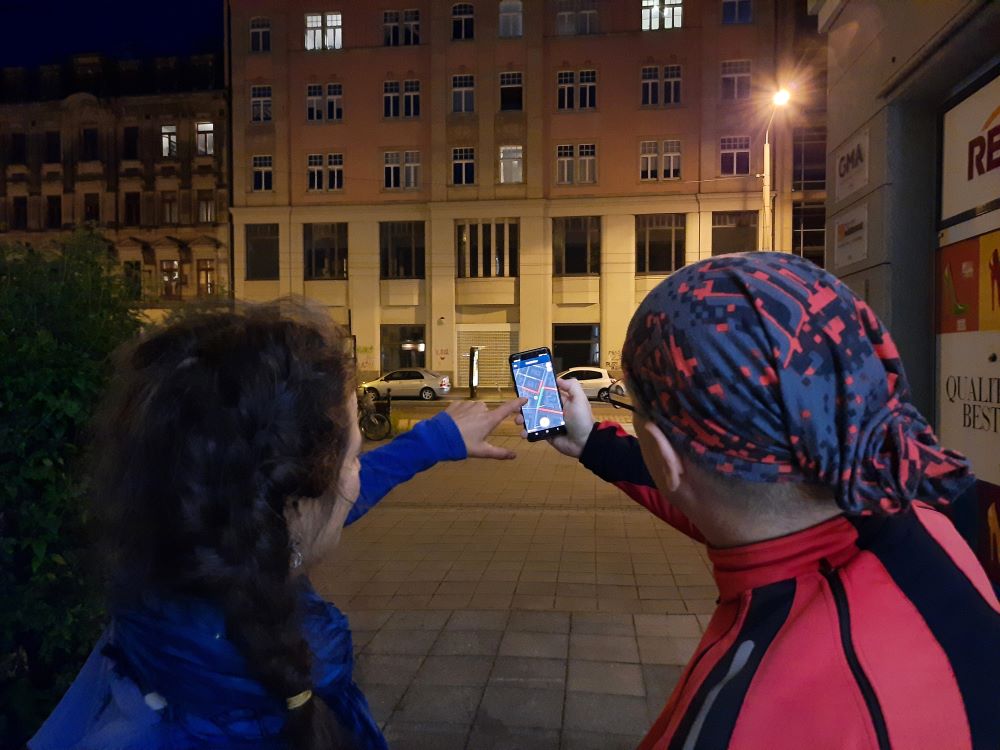 Ein Mann und eine Frau stehen bei Nacht vor einem Haus mit einer Straßenlaterne. Sie stehen mit dem Rücken zur Kamera und halten ein Handy mit der Nachtlicht-App in der Hand. 