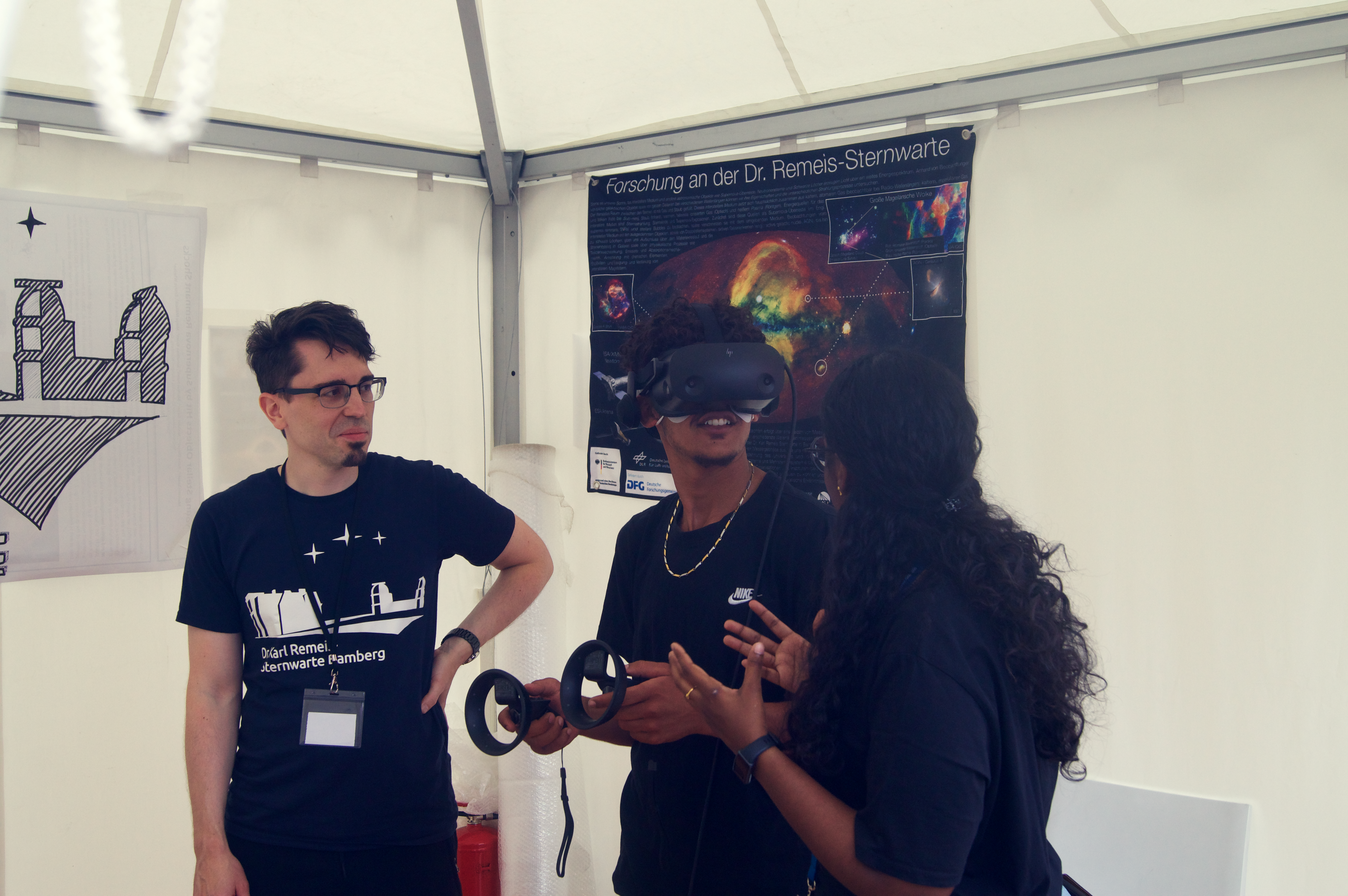 Ein Mann trägt eine VR Brille in einem Zelt, hinter ihm hängt ein Poster von einem Planetarium