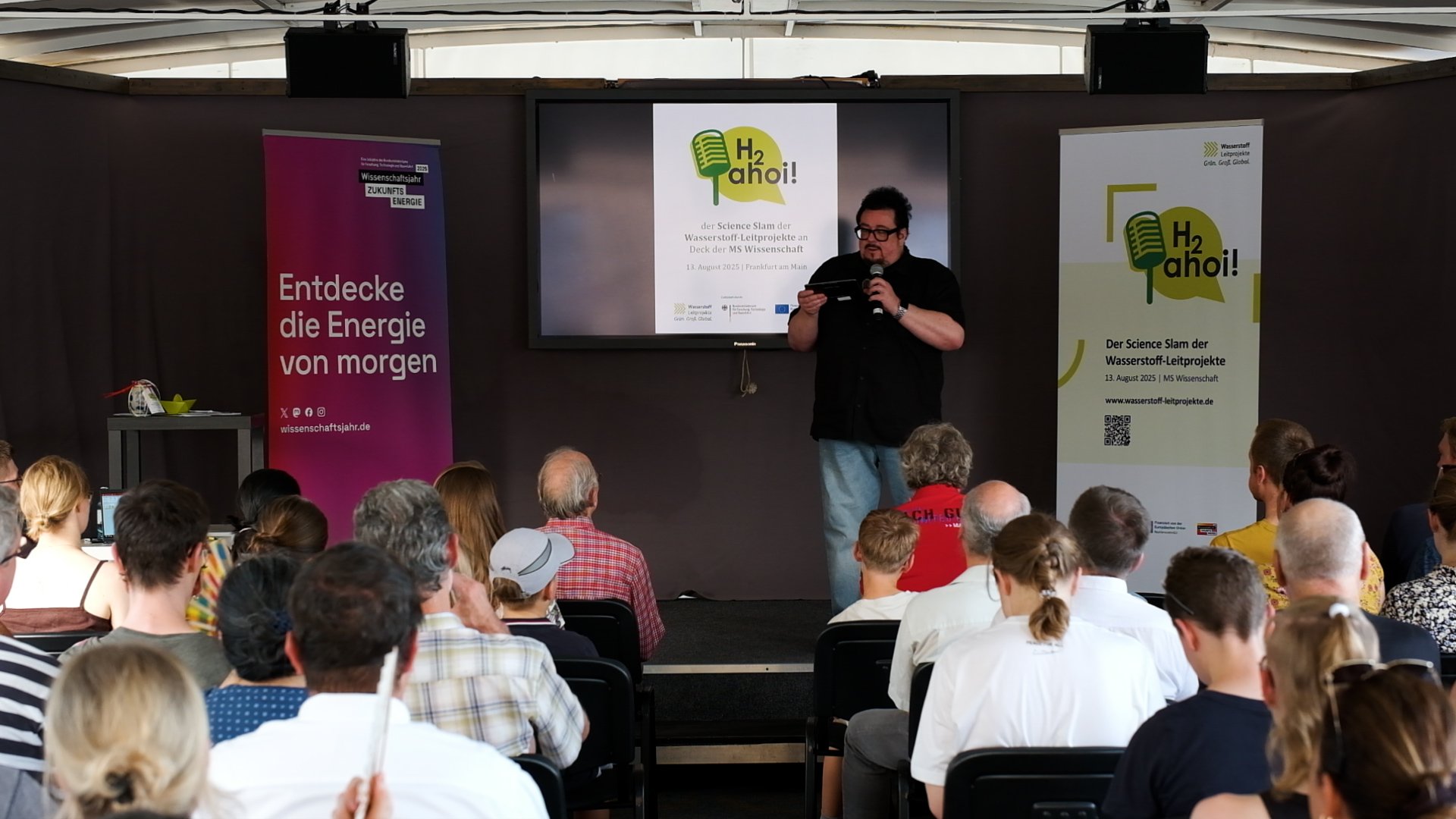 Moderator Martin Stammberger mit Mikrofon vor Publikum.