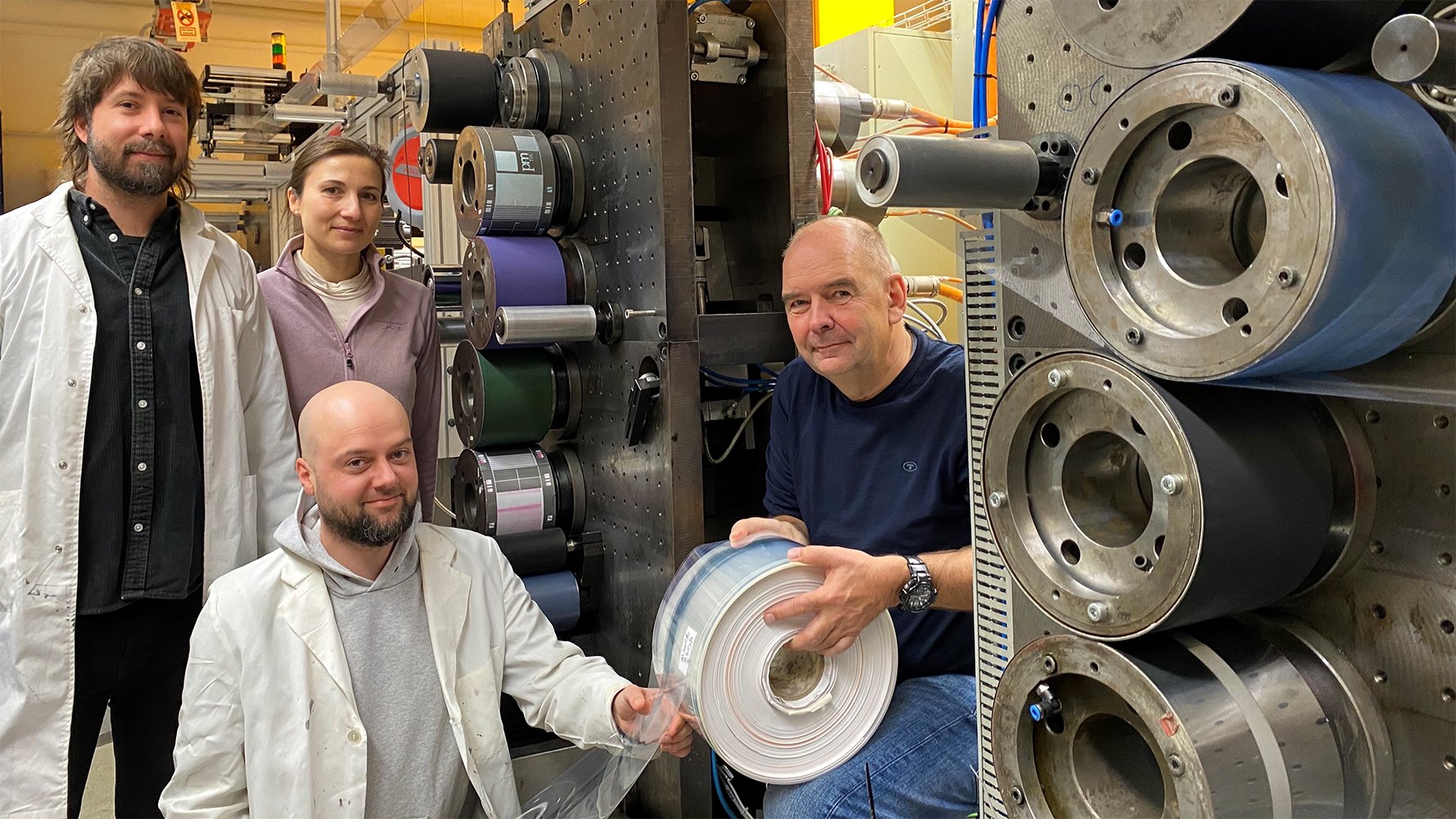 Wissenschaftler an einer Rollendruckmaschine mit dem Testdruck einer leitfähigen Solarzellen-Schicht.