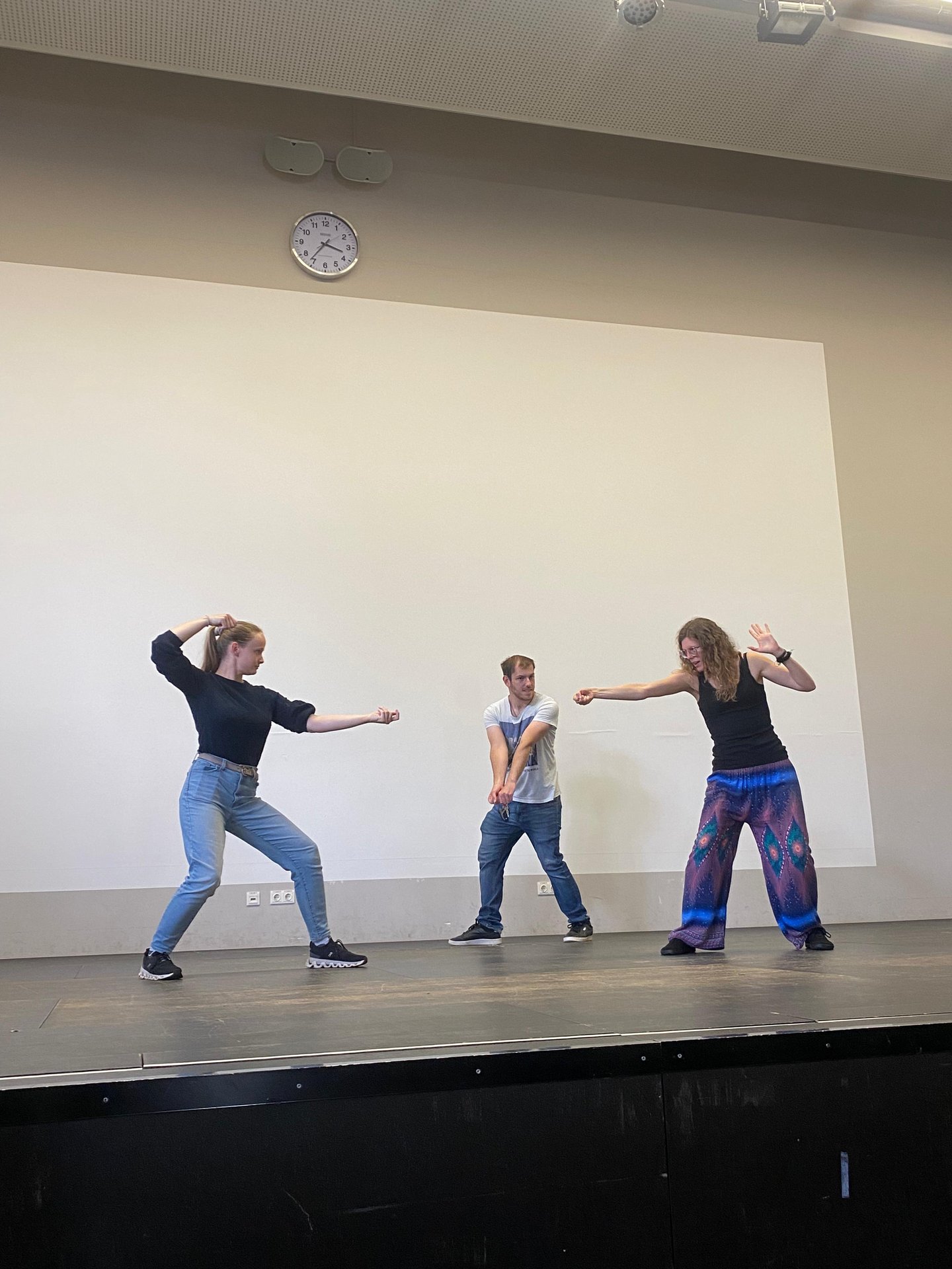 Drei Studierende stellen spielerisch auf der Bühne eine Schwert-Kampfszene nach. 