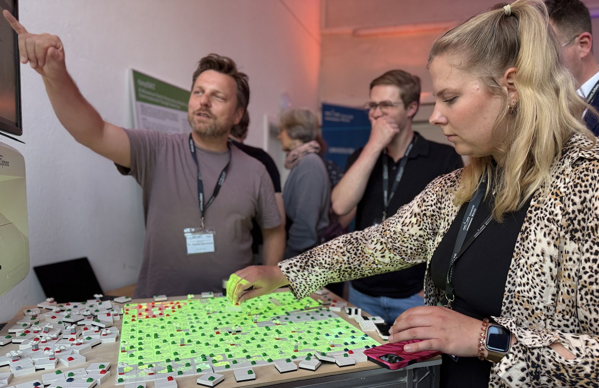 Mehrere Personen tauschen sich vor einem Lego-Windpark-Modell aus und gestikulieren dabei lebhaft.