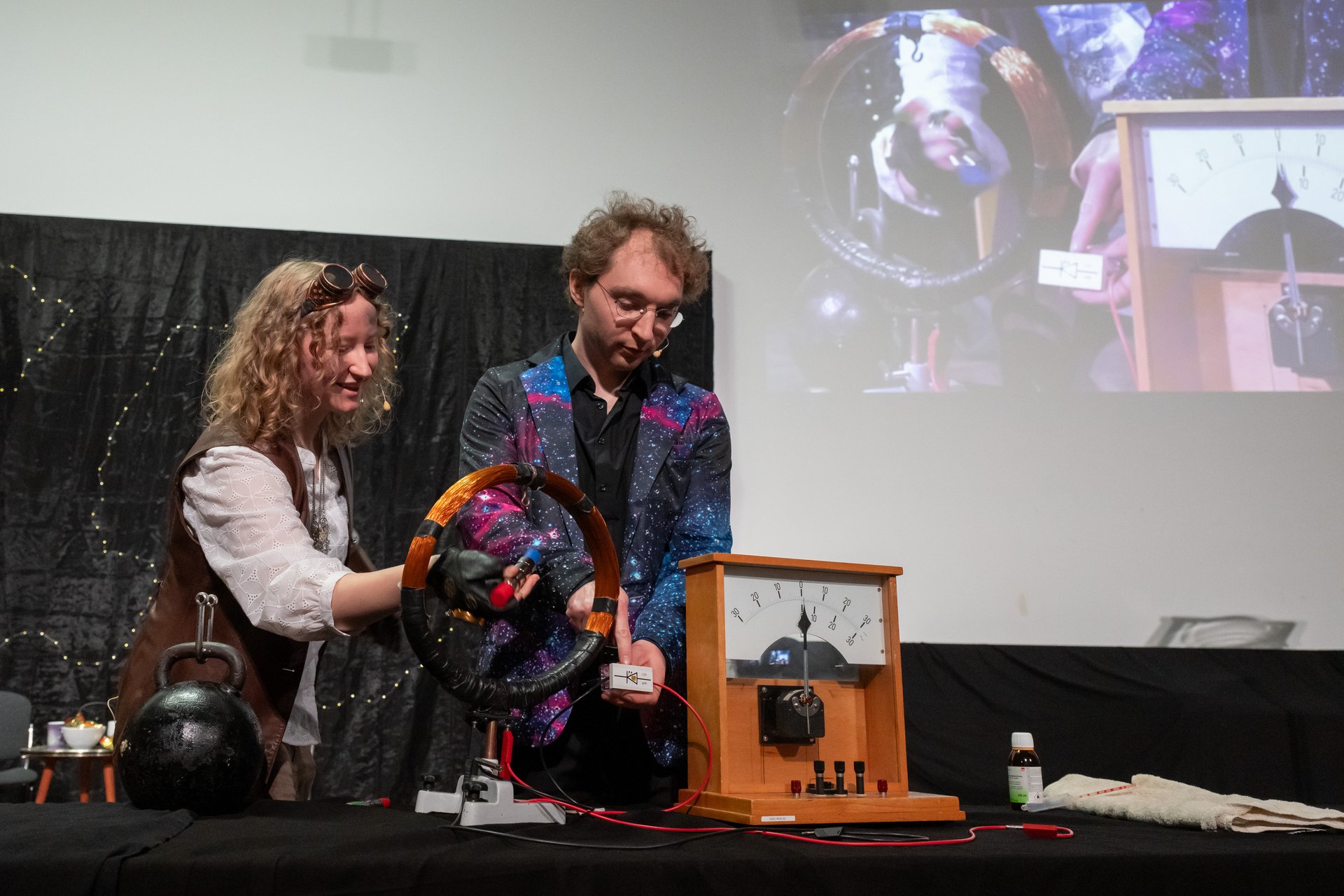 Verkleidete*r Schauspielerin und Schauspieler führen physikalisches Experiment live auf der Bühne durch.