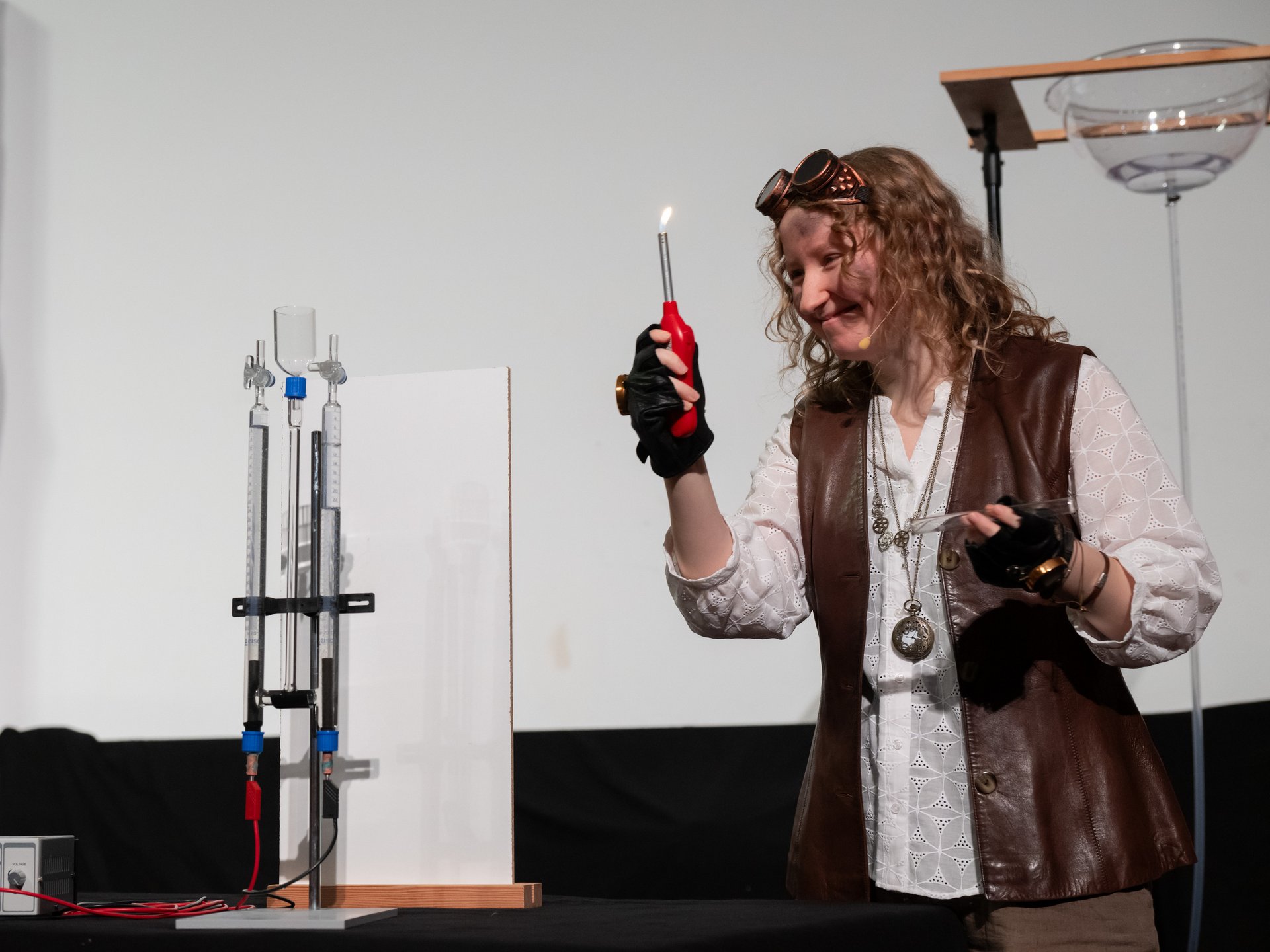 Verkleidete Schauspielerin hält Stabfeuerzeug mit Flamme in der Hand.