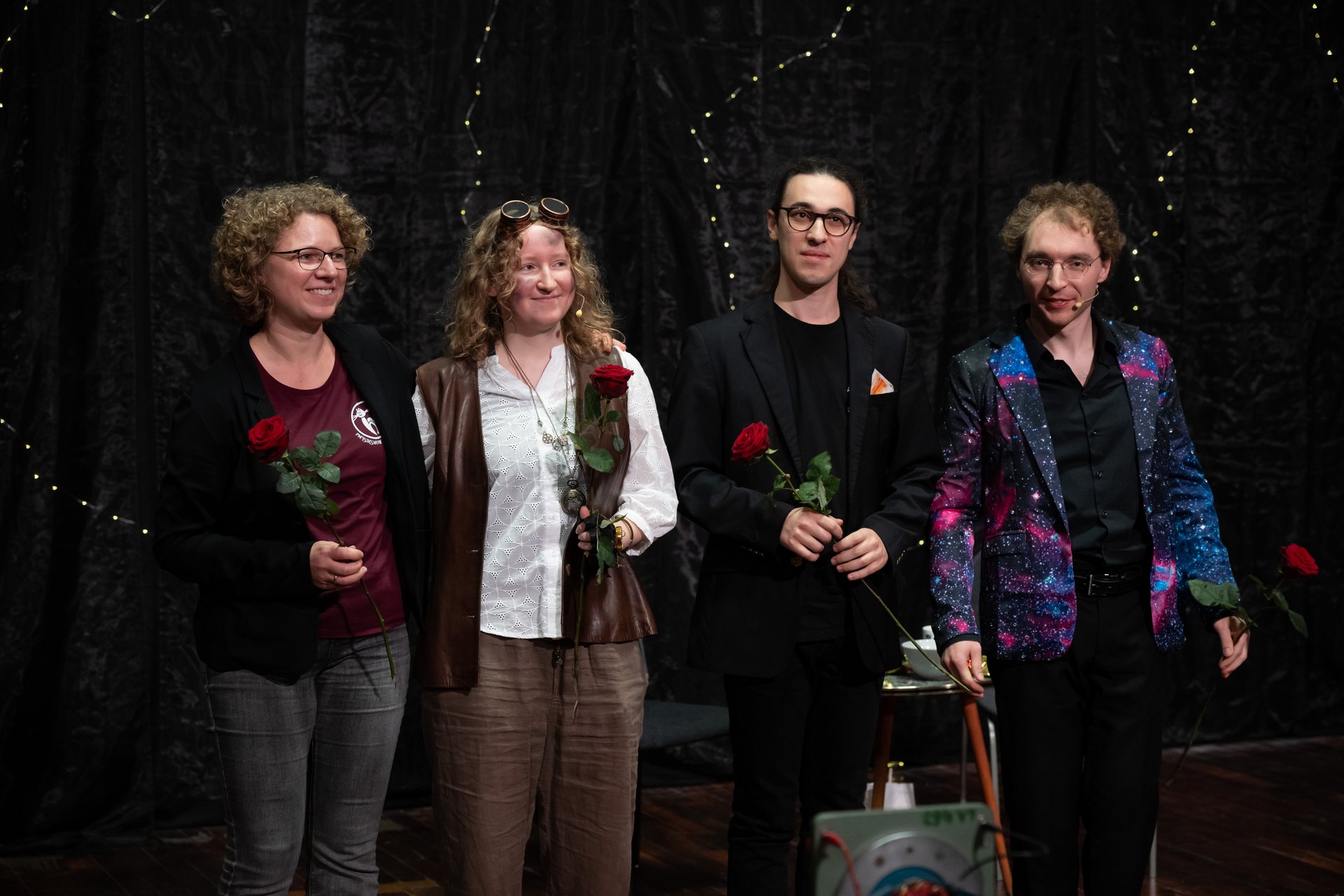 Künstler*innen und Projektverantwortliche stehen am Ende des Stücks auf der Bühne und halten jeweils eine rote Rose in der Hand. 