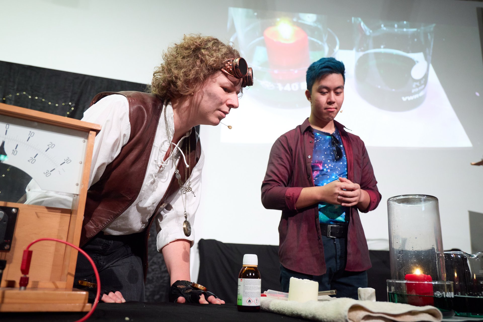 Verkleidete*r Schauspielerin und Schauspieler führen ein Live-Experiment durch. Sie stülpen ein großes Glas über eine Kerze. 