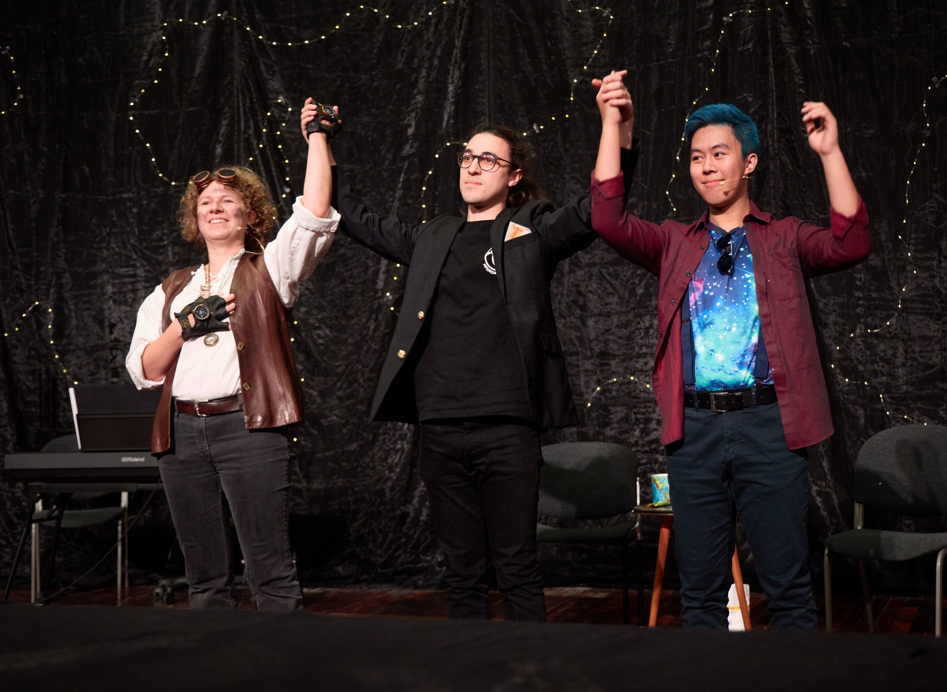 Schauspielerin und Schauspieler stehen am Ende des Stücks auf der Bühne. Eine dritte Person steht zwischen den beiden und hält ehrend die Hände der Schauspieler*innen in die Höhe.