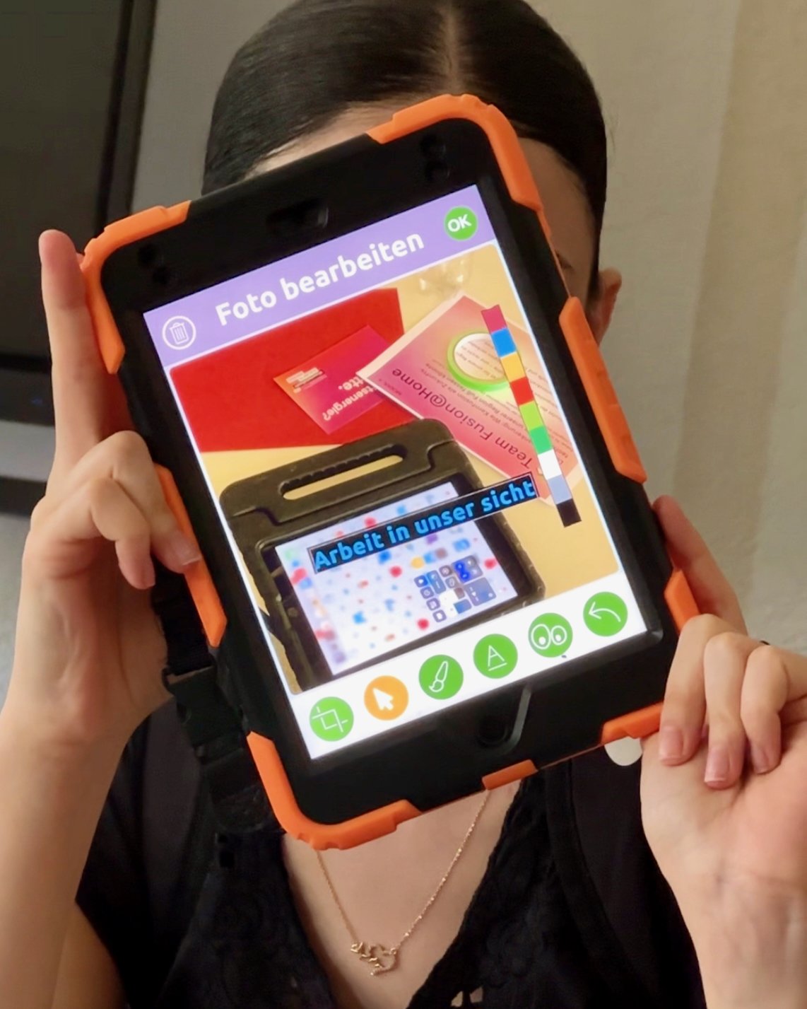 Eine Person hält ein Tablet vor ihr Gesicht, sodass sie nicht zu erkennen ist.