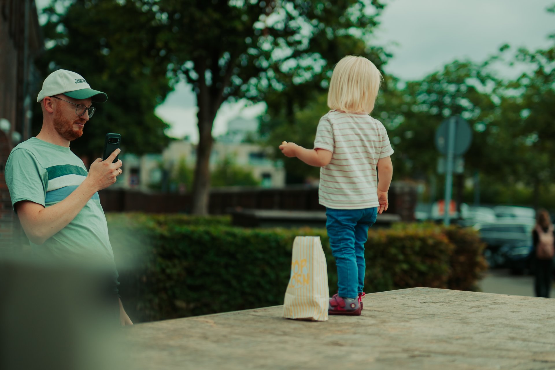 Kind steht auf der Ladefläche eines Autos, ein Mann steht daneben und macht ein Handyfoto von dem Kind.