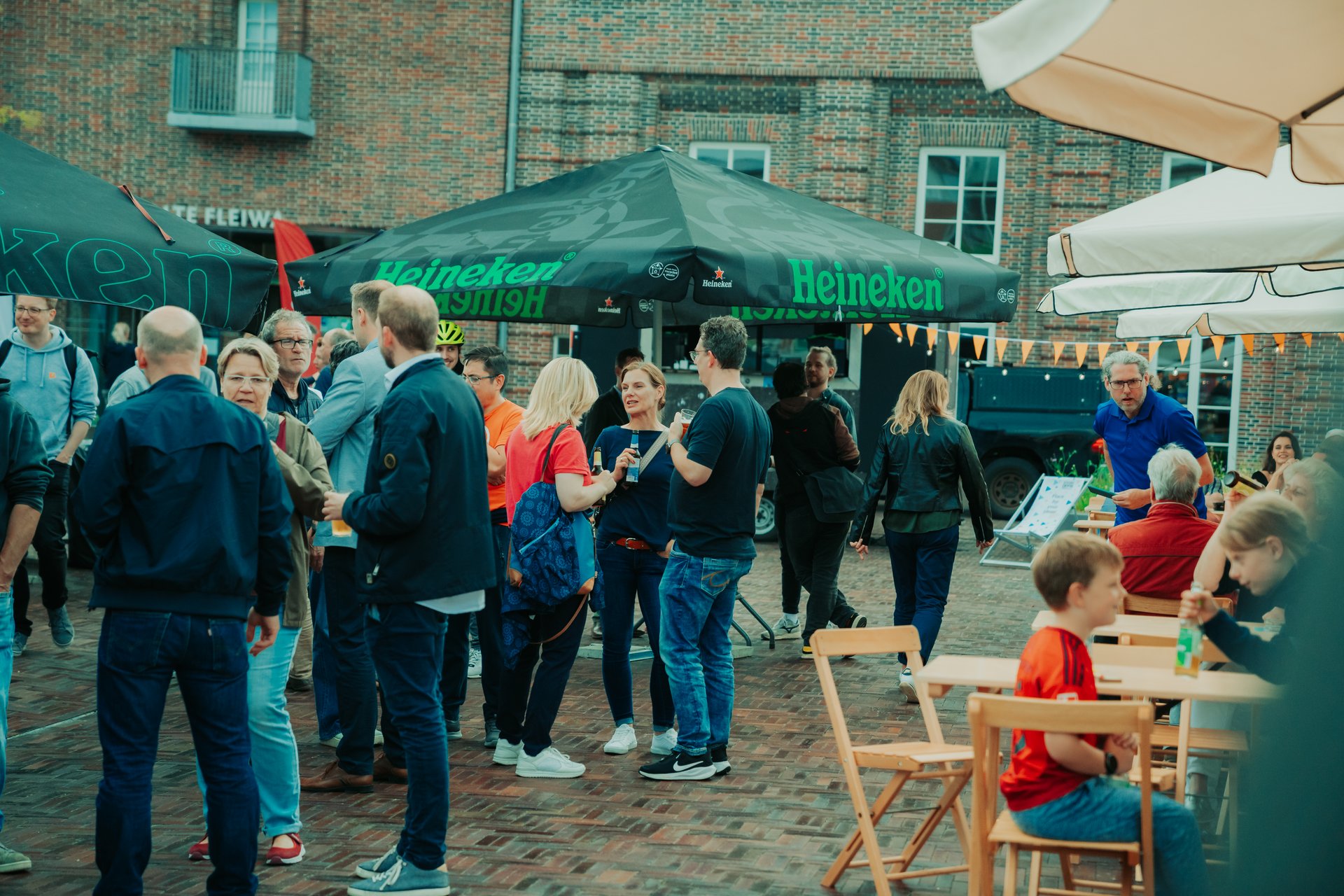 Zahlreiche Menschen stehen auf einem Straßenfest vor Sonnenschirmen und unterhalten sich.