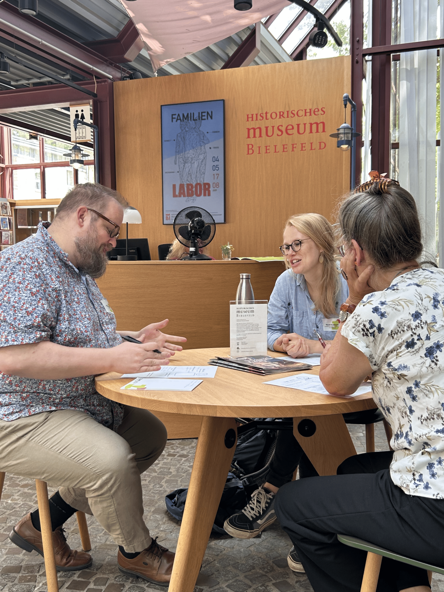 Zwei Frauen und ein Mann diskutieren an einem Tisch im Historischen Museum Bielefeld.