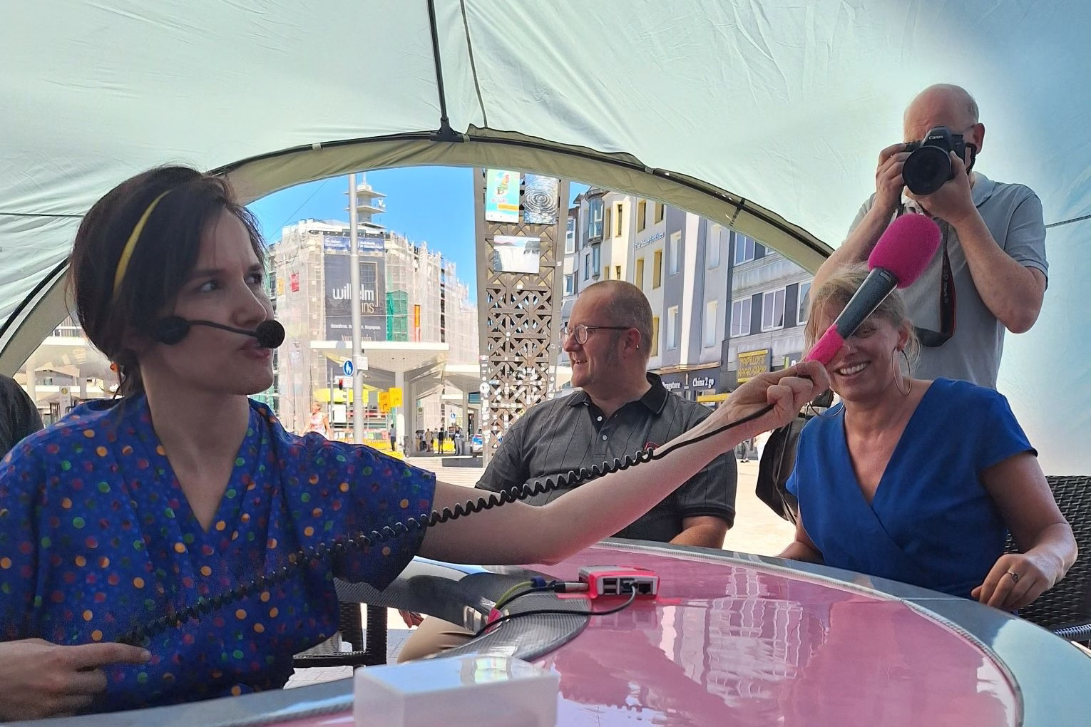 Eine Frau sitzt in der Mitte eines runden Tisches und hält ein Mikrofon zum Tischrand.