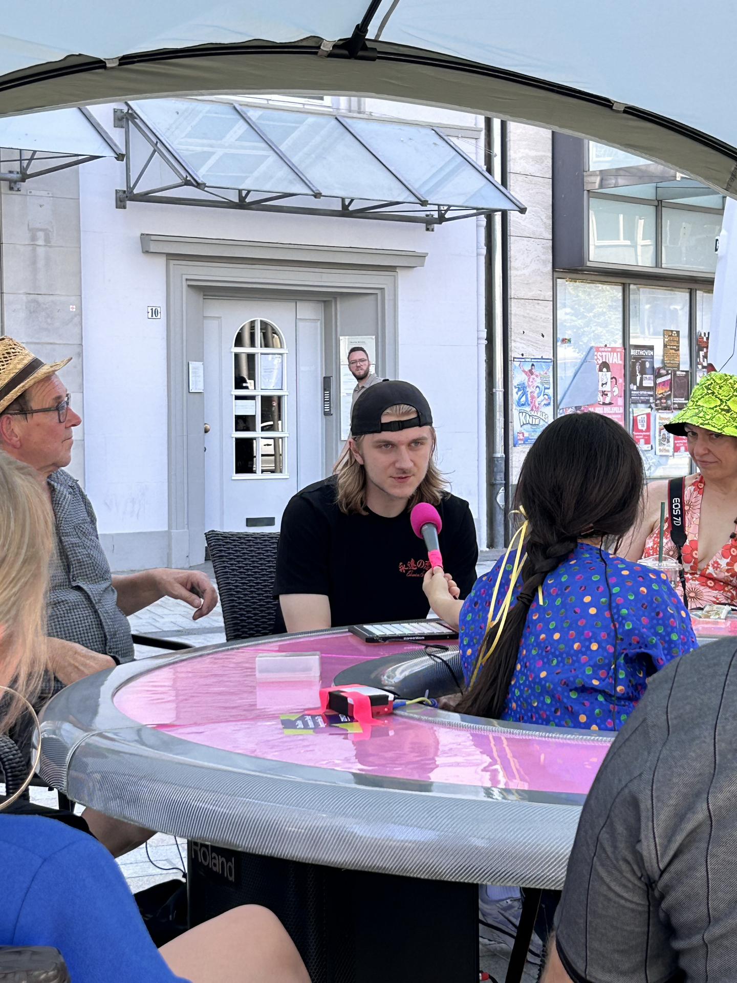 Eine junge Person sitzt mit anderen am runden Tisch und spricht in ein Mikrofon.