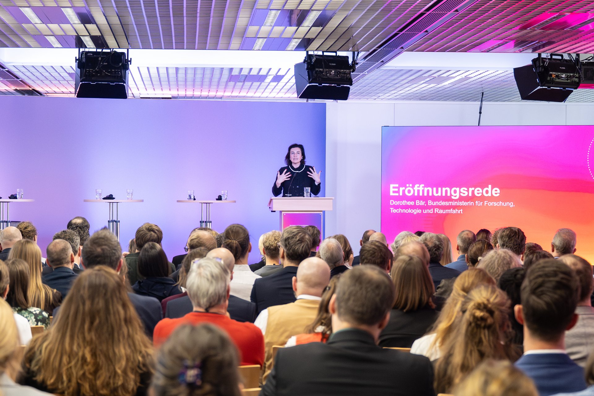 Bundesforschungsministerin Dorothee Bär steht im Hintergrund auf einer Bühne am Rednerpult, im Vordergrund sitzt das Publikum.