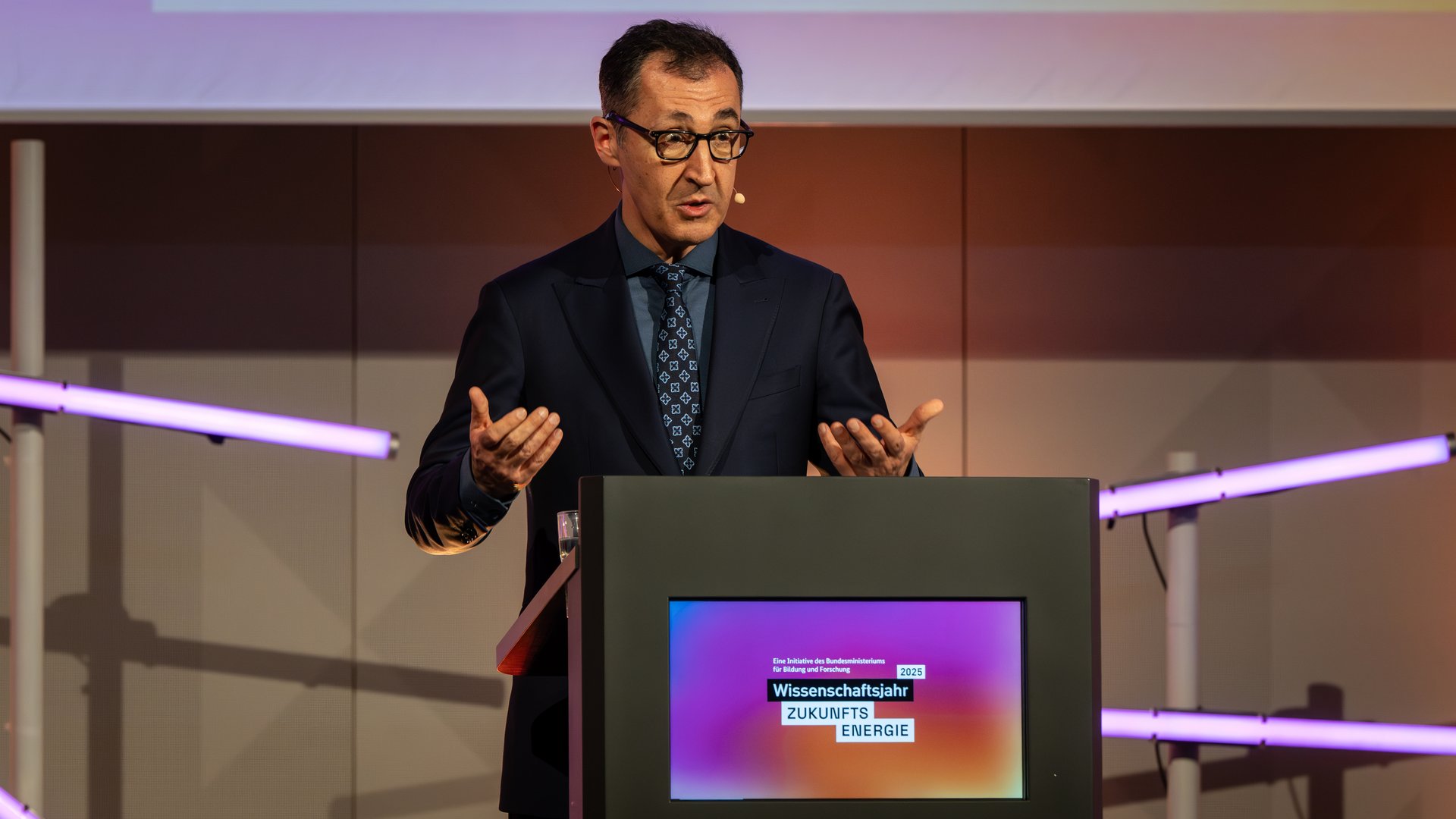 Bundesminister für Bildung und Forschung Cem Özdemir steht an einem Pult und hält eine Rede.