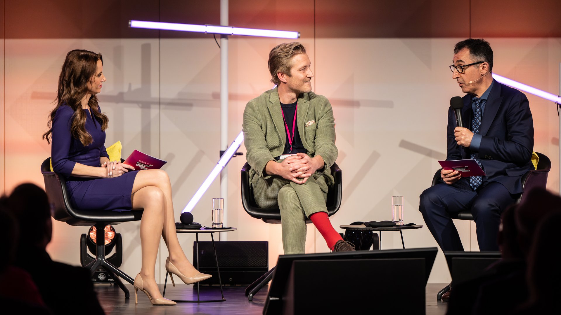 Drei Personen sitzen auf Stühlen auf einer Bühne, Bundesminister für Bildung und Forschung Cem Özdemir spricht in ein Mikrofon.