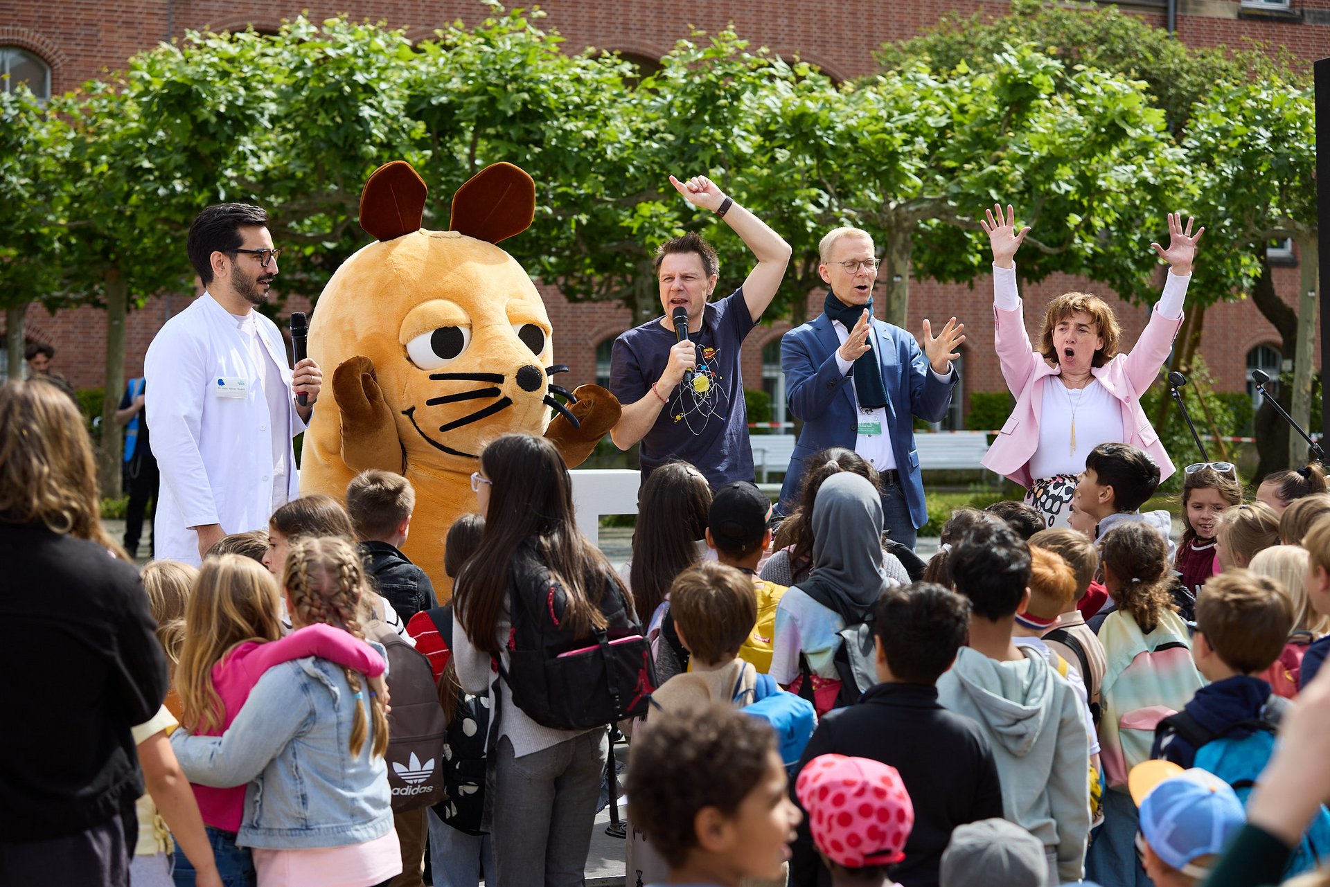 Vier Menschen und die Maus als Walking Act stehen auf einer Bühne im Freien, davor stehen viele Kinder.