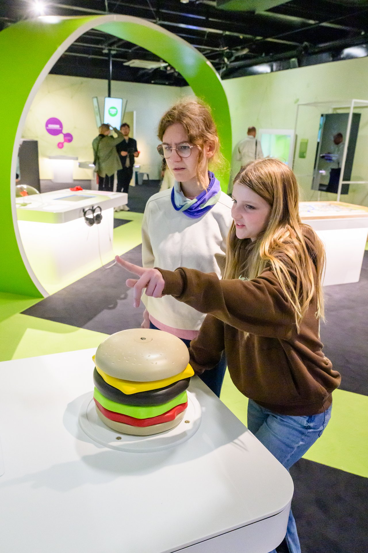 Eine Frau und ein Mädchen stehen vor einem übergroßen Burger aus Plastik.