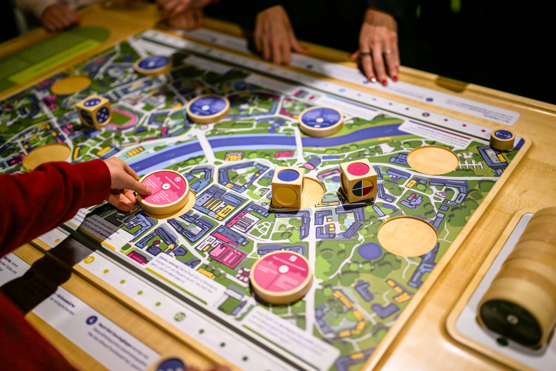 Ein Holzspielbrett, das eine Stadt zeigt. Darauf liegen bunte Würfel und Scheiben.