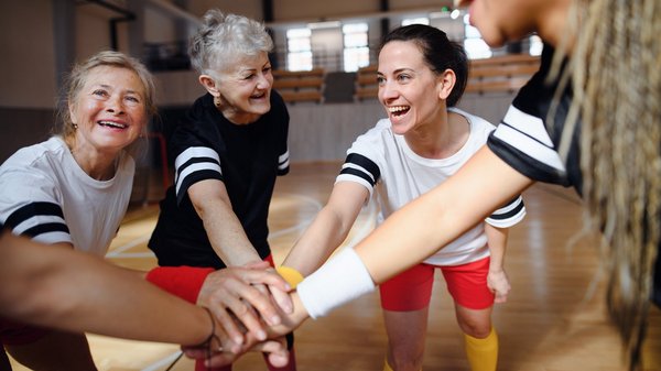 Eine Sportmannschaft aus Frauen unterschiedlichen Alters hält die Hände in ihre Mitte.