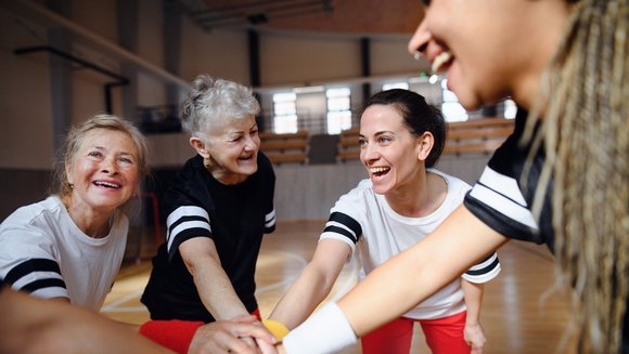 Eine Sportmannschaft aus Frauen unterschiedlichen Alters hält die Hände in ihre Mitte.