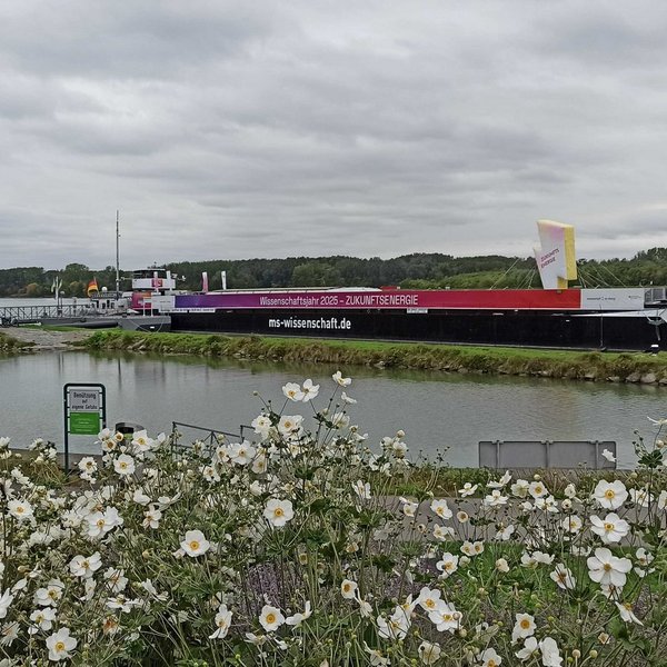 Schiff mit der Aufschrift "Wissenschaftsjahr 2025 – Zukunftsenergie" liegt an einem begrünten Steg vor Anker
