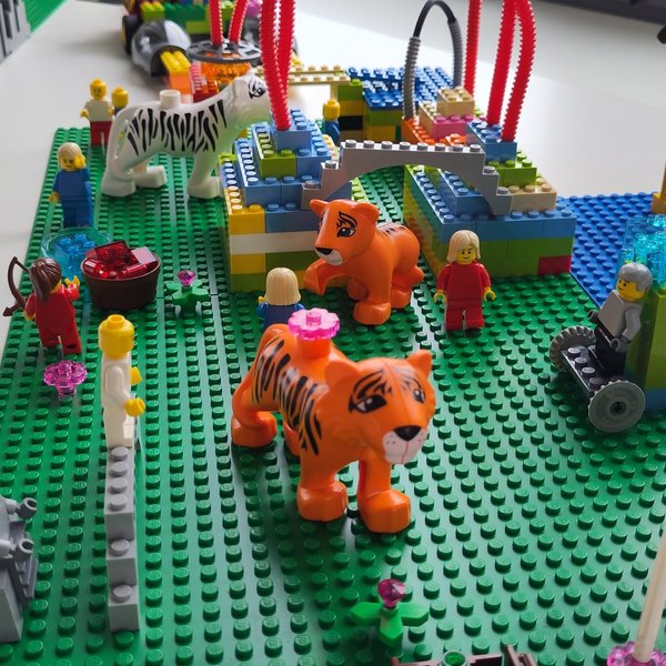 Modell aus Klemmbausteinen mit Blumen, Schläuchen, Figuren und Tigern auf einer Platte
