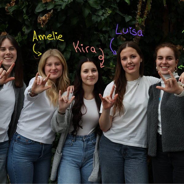 Fünf Teilnehmerinnen von Energiealogue posieren für ein Gruppenfoto und zeigen das internationale Zeichen für Solidarität mit allen Gebärdensprachler:innen. Die Namen der einzelnen Studentinnen stehen über ihren Köpfen - Hanna, Amelie, Kira, Luisa, Hannah.