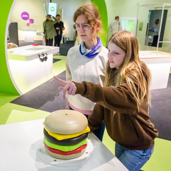 Eine Frau und ein Mädchen stehen vor einem übergroßen Burger aus Plastik.