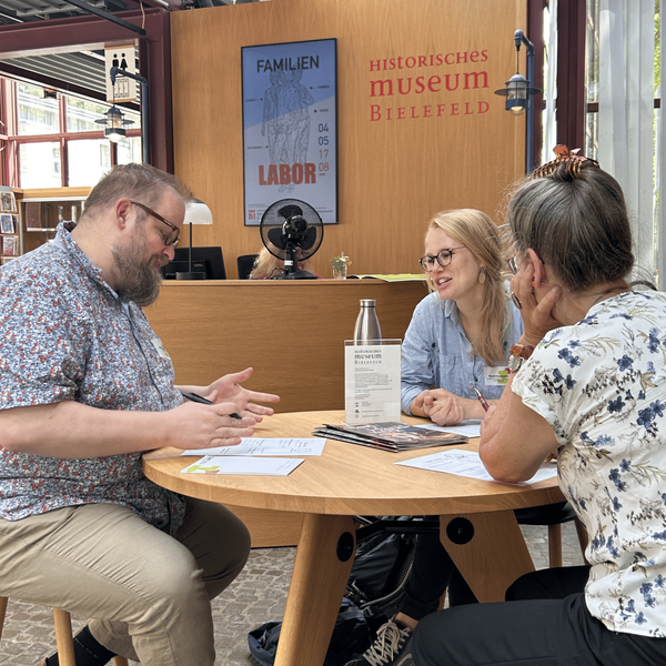 Zwei Frauen und ein Mann diskutieren an einem Tisch im Historischen Museum Bielefeld.