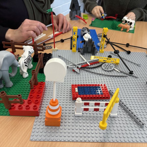 Hände von zwei Personen, die an einem Tisch mit Klemmbausteinen bauen