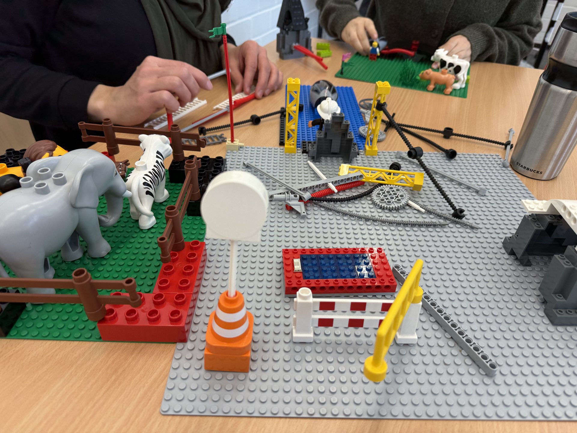 Hände von zwei Personen, die an einem Tisch mit Klemmbausteinen bauen