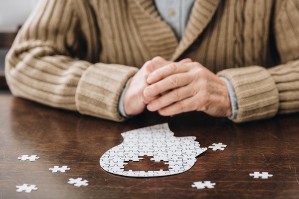Eine ältere Person sitzt vor einem Puzzle eines menschlichen Kopfs.