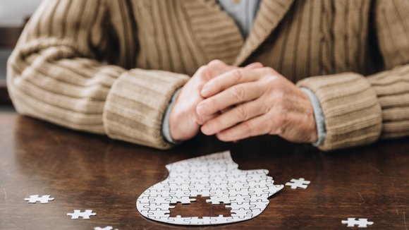 Eine ältere Person sitzt vor einem Puzzle eines menschlichen Kopfs.