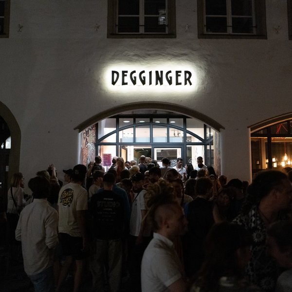 Viele junge Menschen befinden sich abends vor dem Eingang eines Gebäudes mit der Aufschrift "Degginger". 