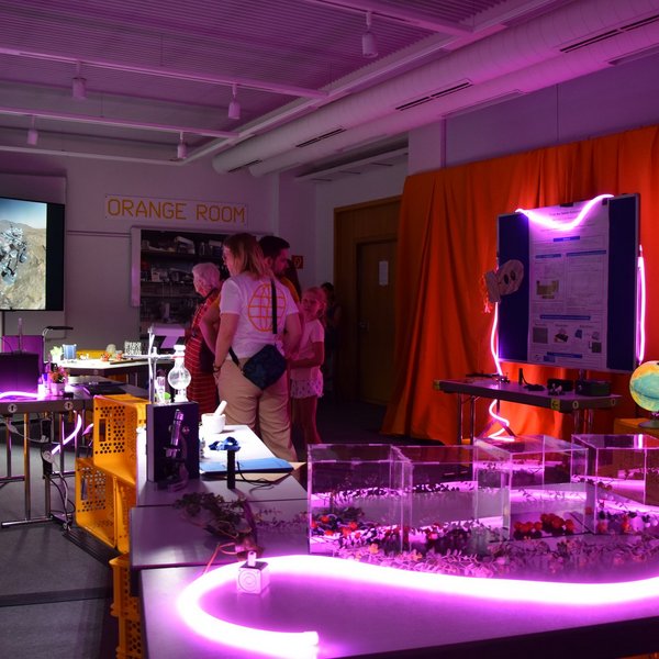 Menschen in einem Escape Room, der mit lila Neonröhren beleuchtet wird.