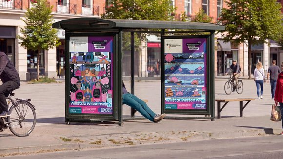 Bushaltestelle mit Plakaten, auf denen Comic-Figuren abgebildet sind und der Text: Willst du wissen wie?