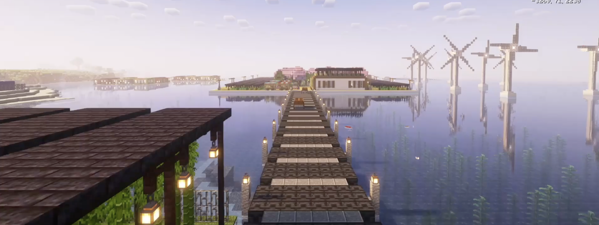 In Minecraft gebauter Steg über Wasser führt zu einer rechteckigen Insel mit Gebäuden, im Wasser stehen Windräder