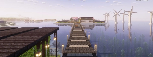 In Minecraft gebauter Steg über Wasser führt zu einer rechteckigen Insel mit Gebäuden, im Wasser stehen Windräder