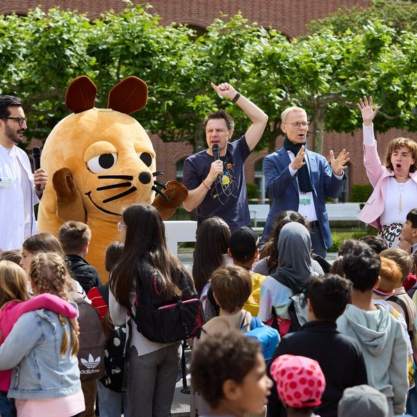 Vier Menschen und die Maus als Walking Act stehen auf einer Bühne im Freien, davor stehen viele Kinder.