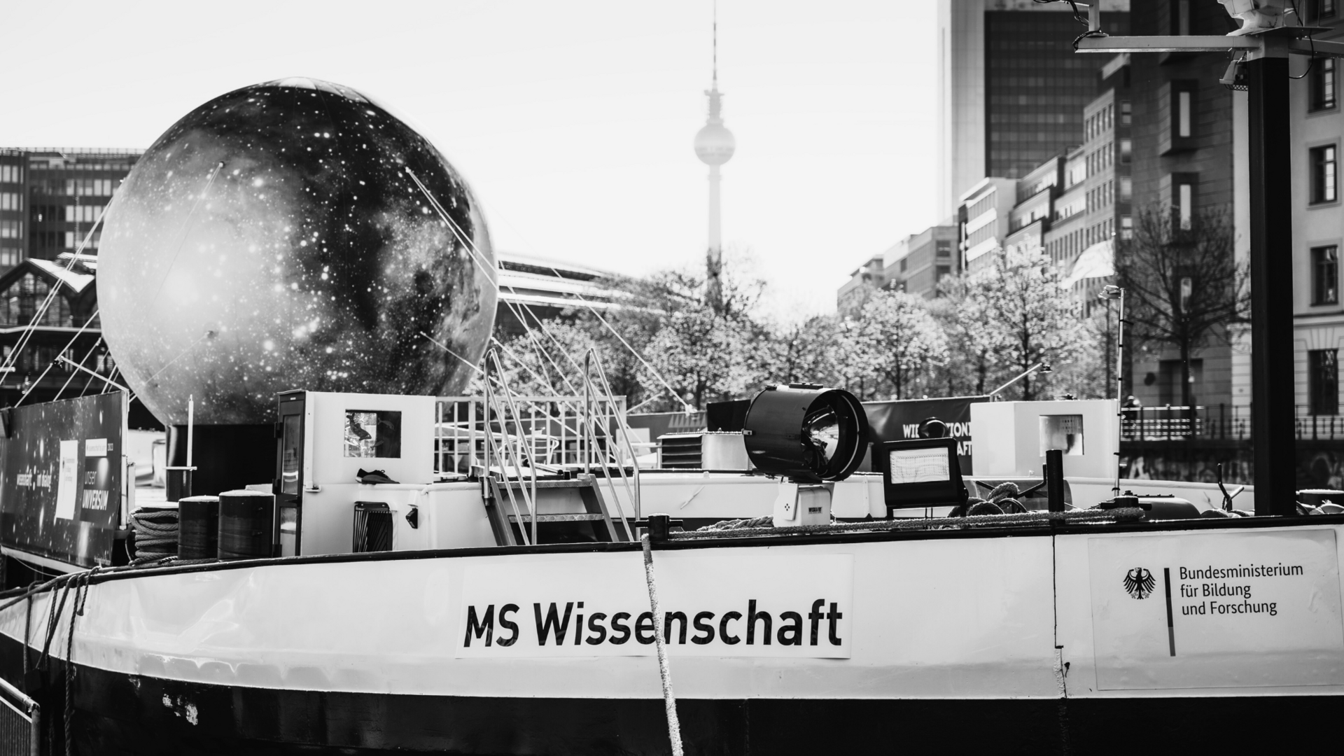Projektbild MS Wissenschaft: Foto eines Frachtschiffes, an der Reling steht "MS Wissenschaft" An Deck ist eine große Attrappe des Mondes mit Seilen befestigt.