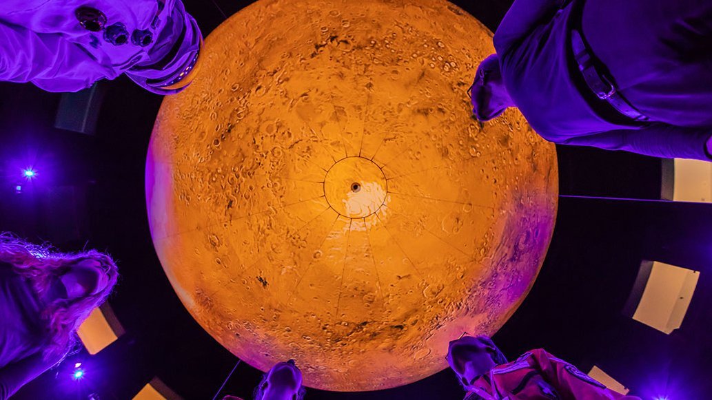 Einige Leute stehen im Kreis um das orange leuchtende Marsmodell