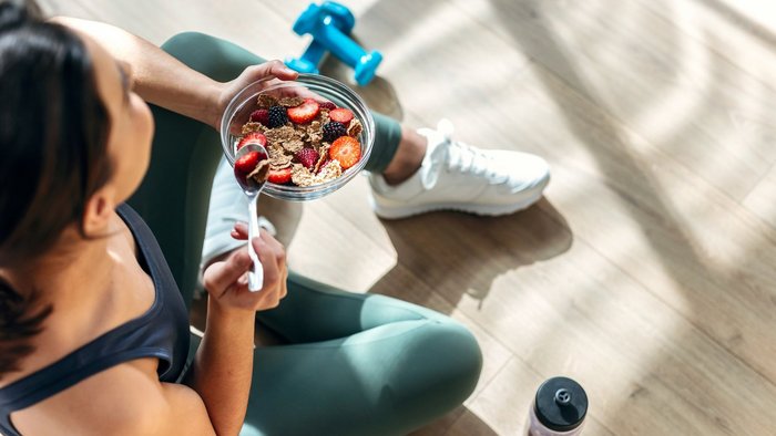 EIne Frau in Sportkleidung isst ein Müsli.