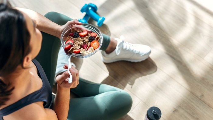 EIne Frau in Sportkleidung isst ein Müsli.