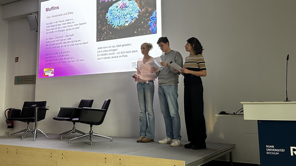 Drei Personen stehen auf einer Bühne vor einer Leinwand mit dem Bild von einem Muffin